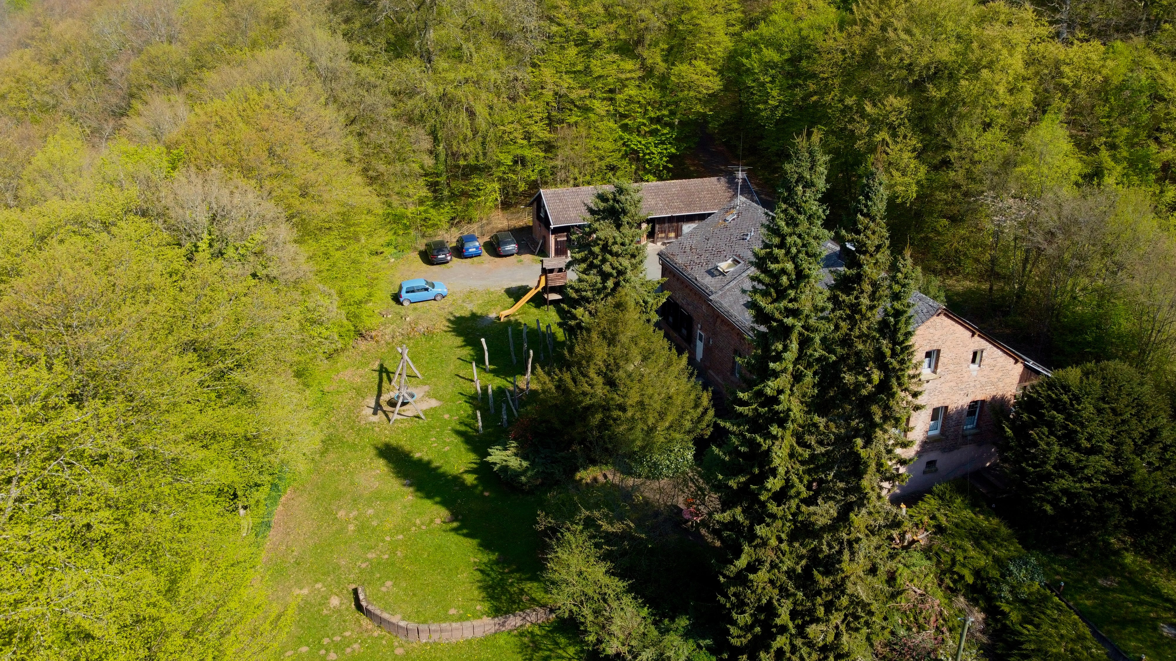 Drohnenblick auf den Spielplatz neben dem Freizeitheim mit Holzspielgeräten und Wiese.